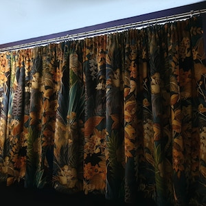 May include: Curtains with a dark blue background and a colorful floral pattern featuring yellow, orange, and green hues. The curtains are hung on a silver curtain rod.