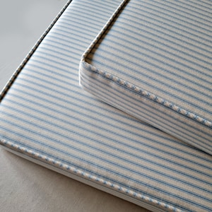 May include: Two striped cushions with blue and white stripes. The cushions are sewn with a white thread and have a white border.