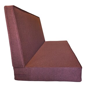 May include: A burgundy-colored, upholstered bench with a backrest. The bench has a rectangular seat and back, with a slightly angled backrest. The fabric appears to be a textured weave.