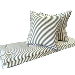 A firm upholstery foam bench cushion made to measure to custom size. The bench cushion cover is made to order in a 100% cotton, natural fabric striped ticking fabric made in the UK. The green and white stripey fabric bench cushion is button tufted with firm foam and dacron inside. The zip at the back of the cushion allows the covers to be removed. Two scatter cushions with eco fibre filling in the same off white and racing green stripe fabric. French chic ticking fabric bench cushion