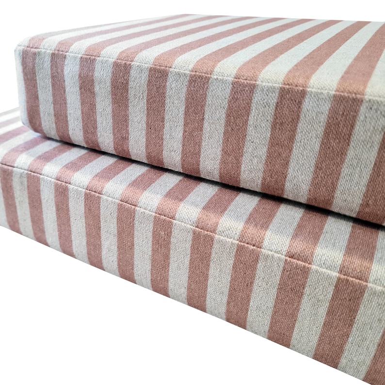 Two thick, high quality bench cushions made with pink and white striped fabric. The candy stripe upholstery fabric is a cotton and linen mix fabric with a natural look. The bench cushions have zips at the back of the cushion covers so they can be removed for cleaning. The modern looking banquette seating cushions have no piping on the edges. The pink and white wide stripe cotton fabric has a stain resistant finish making it perfect for use in kitchens, around kids and pets and children.