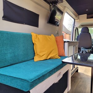 A pull out camper van bed bench cushion set in a teal green blue chenille fabric. The mattress cushions are attached to each other with a fabric join to keep them from falling during transit. The renovated camper van is bright and clean looking. The cushions have zips at the back so the bench cushion covers can be cleaned. Heavy duty velcro on the back of the cushions to keep them in place. Made to measure pull out plywood camper van bed set bespoke high quality, firm supportive foam memory foam