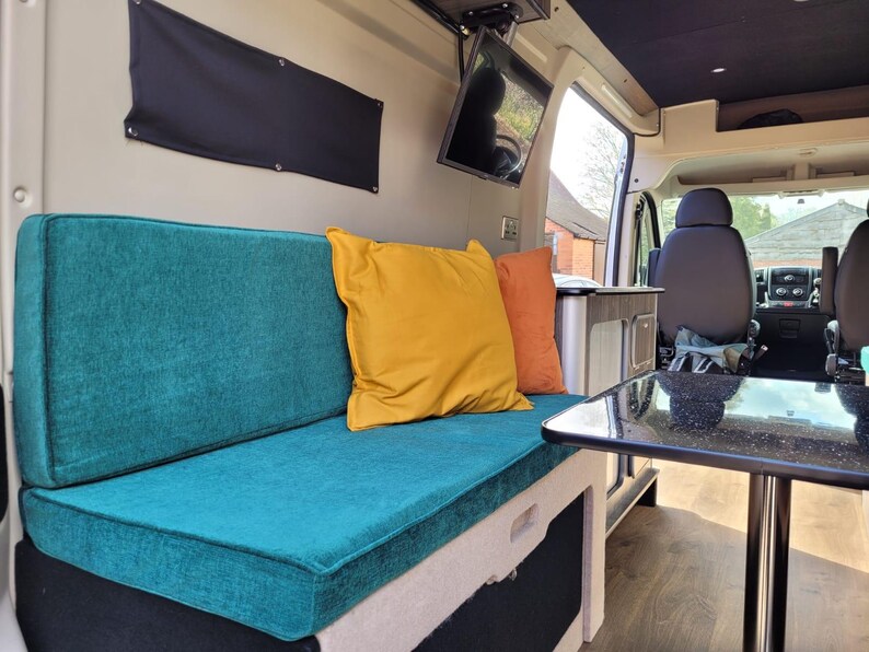 A pull out camper van bed bench cushion set in a teal green blue chenille fabric. The mattress cushions are attached to each other with a fabric join to keep them from falling during transit. The renovated camper van is bright and clean looking. The cushions have zips at the back so the bench cushion covers can be cleaned. Heavy duty velcro on the back of the cushions to keep them in place. Made to measure pull out plywood camper van bed set bespoke high quality, firm supportive foam memory foam