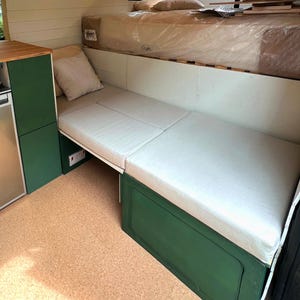 A converted camper van interior with a fold out bed with made to measure mattress cushions. The eco friendly, plastic free kids bedding for a camper van have latex rubber foam inside with natural fire retardant and no chemicals. The motorhome cushions have covers made with cotton fabric which is breathable and natural. The bespoke pull out bed cushions have zips at the back. Platform bed cushions for vw sprinter van models. Wipe clean fabric, pet friendly, easy clean van cushions for bed foam