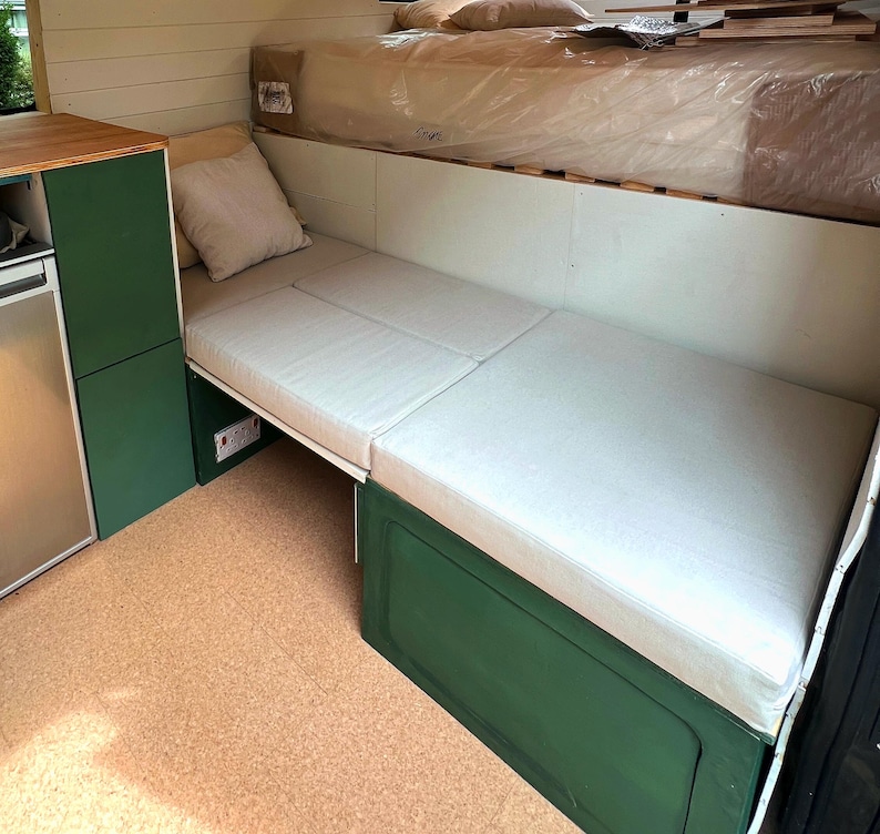 A converted camper van interior with a fold out bed with made to measure mattress cushions. The eco friendly, plastic free kids bedding for a camper van have latex rubber foam inside with natural fire retardant and no chemicals. The motorhome cushions have covers made with cotton fabric which is breathable and natural. The bespoke pull out bed cushions have zips at the back. Platform bed cushions for vw sprinter van models. Wipe clean fabric, pet friendly, easy clean van cushions for bed foam