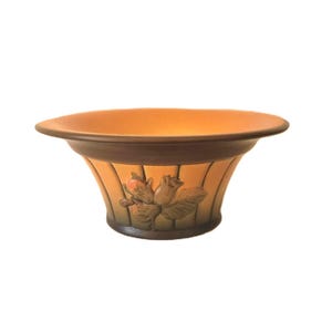 May include: A wide, shallow ceramic bowl with a flared rim, featuring a gradient of warm orange to dark brown tones. The exterior is decorated with a raised, molded relief of a cluster of hazelnuts and leaves, set against vertical fluted panels.