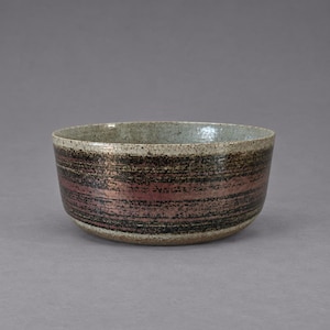Peut inclure: Un bol en céramique rond présentant un intérieur gris clair moucheté et un extérieur texturé avec des bandes horizontales dans des tons brun foncé, noir et rose rougeâtre atténué. Le bol possède une ouverture large et une base arrondie.