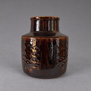 Peut inclure: Un vase cylindrique en céramique avec une glaçure brun foncé très brillante. Le corps présente un motif en losange gaufré répétitif sur l'extérieur, tandis que le col est lisse et droit, menant à une ouverture circulaire simple au sommet.