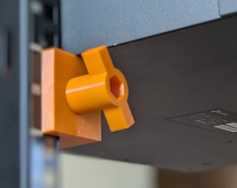 May include: A black network switch mounted on a rack with orange brackets. The switch has multiple ports and is secured with screws. The brackets are a bright orange color and appear to be 3D printed. The rack is black and has vertical rails.
