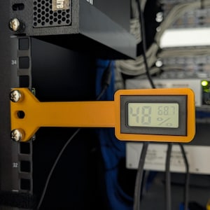 May include: An orange digital temperature and humidity sensor is mounted on a black server rack. The display shows 48% humidity and 68.7 degrees. The sensor is attached with screws.