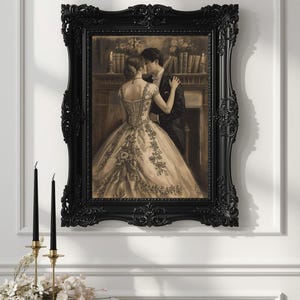 May include: A sepia-toned framed print depicts a couple in formal attire embracing. The woman wears a detailed gown, and the man is in a suit. The black ornate frame complements the romantic scene. Two black candles in gold holders and flowers are in the foreground.
