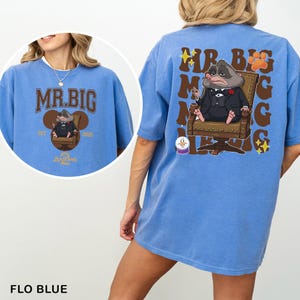 A blue t-shirt with a cartoon image of a raccoon sitting in a chair and the text "MR.BIG" printed on it.