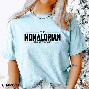 A woman wearing a light blue t-shirt with the text "THE MOMALORIAN THIS IS THE WAY" printed on it.