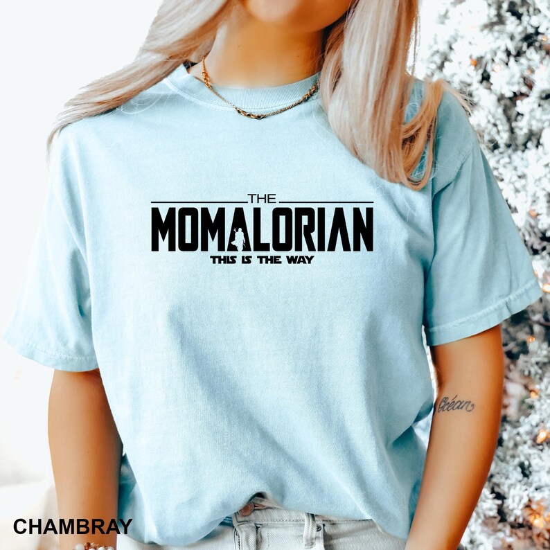 A woman wearing a light blue t-shirt with the text "THE MOMALORIAN THIS IS THE WAY" printed on it.