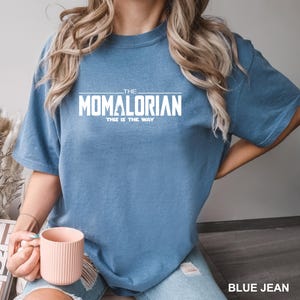 A person wearing a blue t-shirt with the text "THE MOMALORIAN THIS IS THE WAY" printed on it, along with a pink mug in their hand.