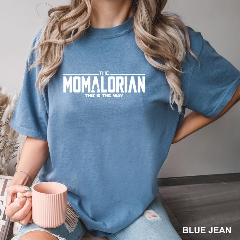 A person wearing a blue t-shirt with the text "THE MOMALORIAN THIS IS THE WAY" printed on it, along with a pink mug in their hand.