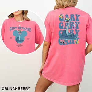A pink t-shirt with a graphic of a cartoon snake and the text "GARY DE SNAKE" printed on it.
