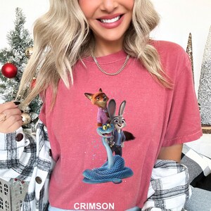 A woman wearing a pink t-shirt with a graphic of a fox, rabbit, and snake.