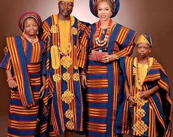 Puede incluir: Una familia de cuatro posa con trajes tradicionales nigerianos a juego. Los atuendos presentan rayas verticales azules, amarillas y rojas. Cada persona lleva un sombrero o pañuelo a juego y collares de cuentas. La ropa tiene detalles bordados en oro.