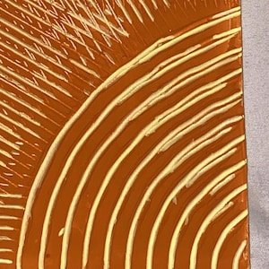 May include: An abstract artwork featuring a warm orange background with a curved, layered design in cream-colored lines. The piece has a textured appearance, with the lines creating a sense of depth and movement. The overall aesthetic is modern and artistic.