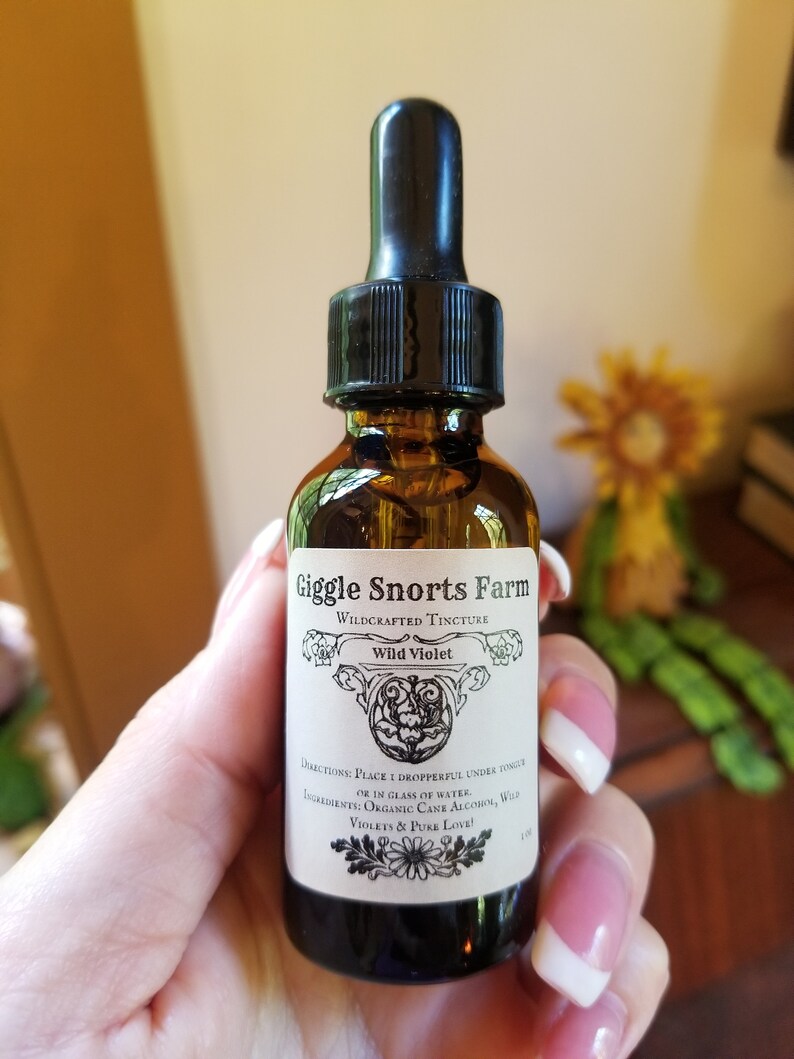 Puede incluir: Una peque&ntilde;a botella de vidrio marr&oacute;n con un gotero negro. La botella est&aacute; etiquetada con "Giggle Snorts Farm Wildcrafted Tincture Wild Violet". La etiqueta tambi&eacute;n incluye instrucciones de uso e ingredientes: "Place 1 dropperful under tongue or in glass of water. Ingredients: Organic Cane Alcohol, Wild Violets & Pure Love!"