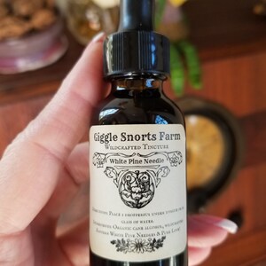 K&ouml;nnte beinhalten: Eine dunkelbraune Glasflasche mit schwarzem Tropfer. Die Flasche ist mit "Giggle Snorts Farm Wildcrafted Tincture White Pine Needle" beschriftet. Das Etikett enth&auml;lt auch Gebrauchsanweisungen und Zutaten.