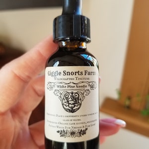 K&ouml;nnte beinhalten: Eine Glasflasche mit Tropfer, die eine dunkle Fl&uuml;ssigkeit enth&auml;lt. Das Etikett lautet "Giggle Snorts Farm Wildcrafted Tincture White Pine Needle". Das Etikett enth&auml;lt auch Gebrauchsanweisungen und Zutaten, darunter Bio-Rohrzuckeralkohol, wildgewachsene Wei&szlig;kiefernnadeln und reine Liebe.