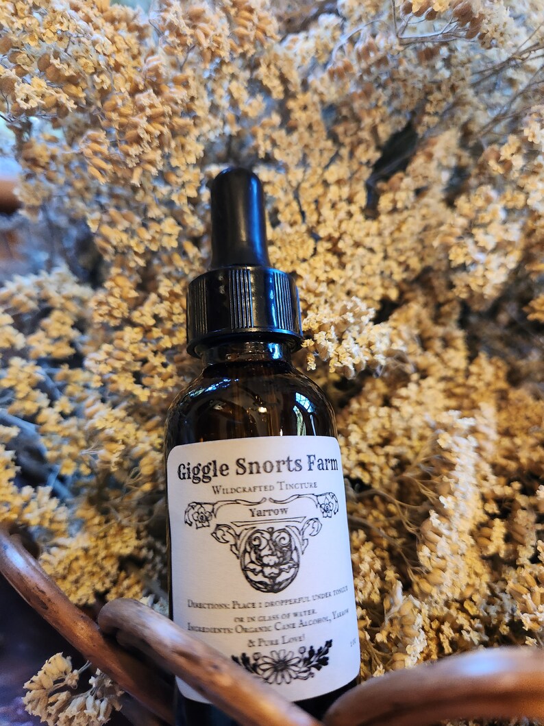 May include: A glass bottle with a dropper top, labeled "Giggle Snorts Farm Wildcrafted Tincture Yarrow". The bottle is sitting in a basket of dried flowers.