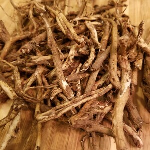 May include: A pile of dried, brown roots on a wooden chopping board. The roots are long and thin, with a rough texture.