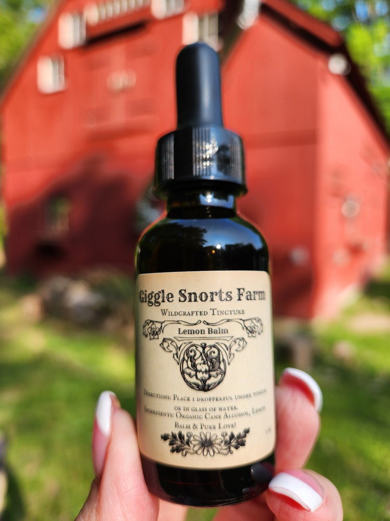 May include: A glass bottle with a dropper top, labeled "Giggle Snorts Farm Wildcrafted Tincture Lemon Balm". The label has a floral design and the text "Directions: Place 1 dropperful under tongue or in glass of water. Ingredients: Organic Cane Alcohol, Lemon Balm & Pure Love!"