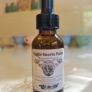 Puede incluir: Una botella de vidrio marr&oacute;n con un gotero negro. La botella est&aacute; etiquetada con "Giggle Snorts Farm Wildcrafted Tincture Wild Violet". La etiqueta tambi&eacute;n incluye instrucciones de uso e ingredientes: "Place dropperful under tongue or in glass of water. Ingredients: Organic Cane Alcohol, Wild Violets & Pure Love!"