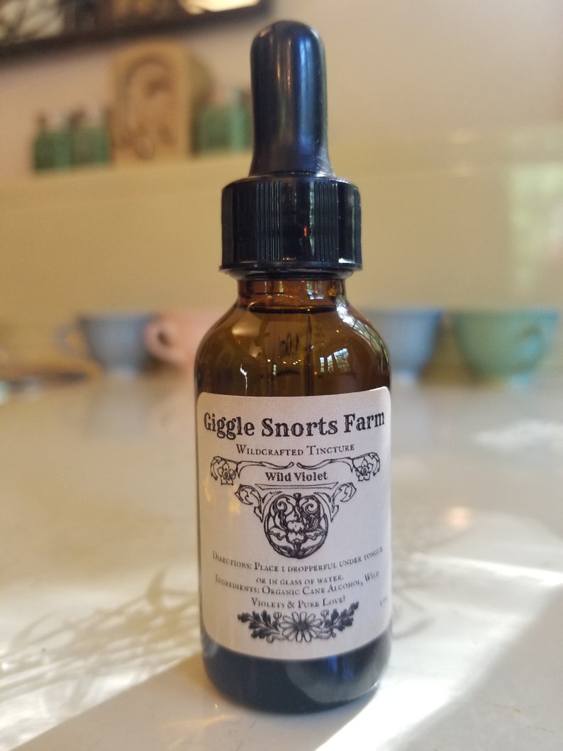 Puede incluir: Una botella de vidrio marr&oacute;n con un gotero negro. La botella est&aacute; etiquetada con "Giggle Snorts Farm Wildcrafted Tincture Wild Violet". La etiqueta tambi&eacute;n incluye instrucciones de uso e ingredientes: "Place dropperful under tongue or in glass of water. Ingredients: Organic Cane Alcohol, Wild Violets & Pure Love!"