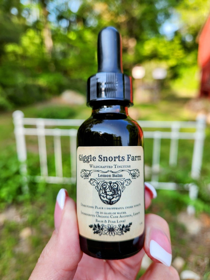 May include: A small glass bottle with a dropper top, labeled "Giggle Snorts Farm Wildcrafted Tincture Lemon Balm". The label has a floral design and the text "Directions: Place 1 dropperful under tongue or in glass of water. Ingredients: Organic Cane Alcohol, Lemon Balm & Pure Love!"