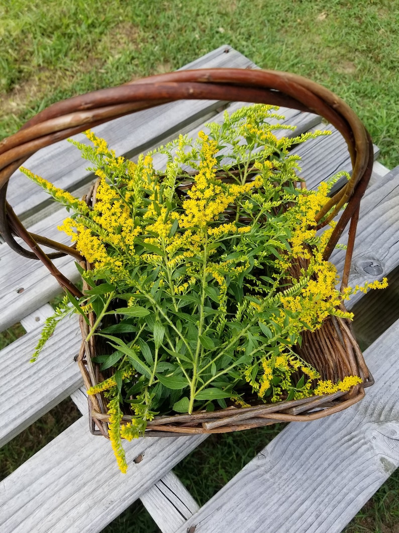 Puede incluir: Una cesta de mimbre llena de un ramo de flores silvestres amarillas. La cesta est&aacute; sobre una superficie de madera.