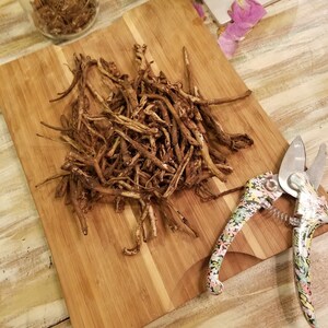 May include: A pile of dried brown roots on a wooden chopping board with a floral patterned pruning shears.
