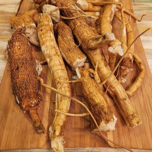 May include: A close-up of a pile of brown, knobby roots on a wooden cutting board. The roots are arranged in a haphazard manner, with some of them overlapping.