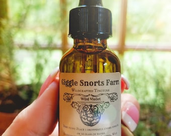 May include: A brown glass bottle with a black dropper top and a white label that reads "Giggle Snorts Farm Wildcrafted Tincture Wild Violet". The label also includes directions for use and ingredients, which are "Organic Cane Alcohol, Wild Violets & Pure Love!"