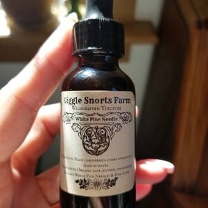 K&ouml;nnte beinhalten: Eine Glasflasche mit Tropfer und einem wei&szlig;en Etikett, auf dem "Giggle Snorts Farm Wildcrafted Tincture White Pine Needle" steht. Das Etikett enth&auml;lt auch Gebrauchsanweisungen und Zutaten, n&auml;mlich "Organic Cane Alcohol, Wildcrafted Eastern White Pine Needles & Pure Love".