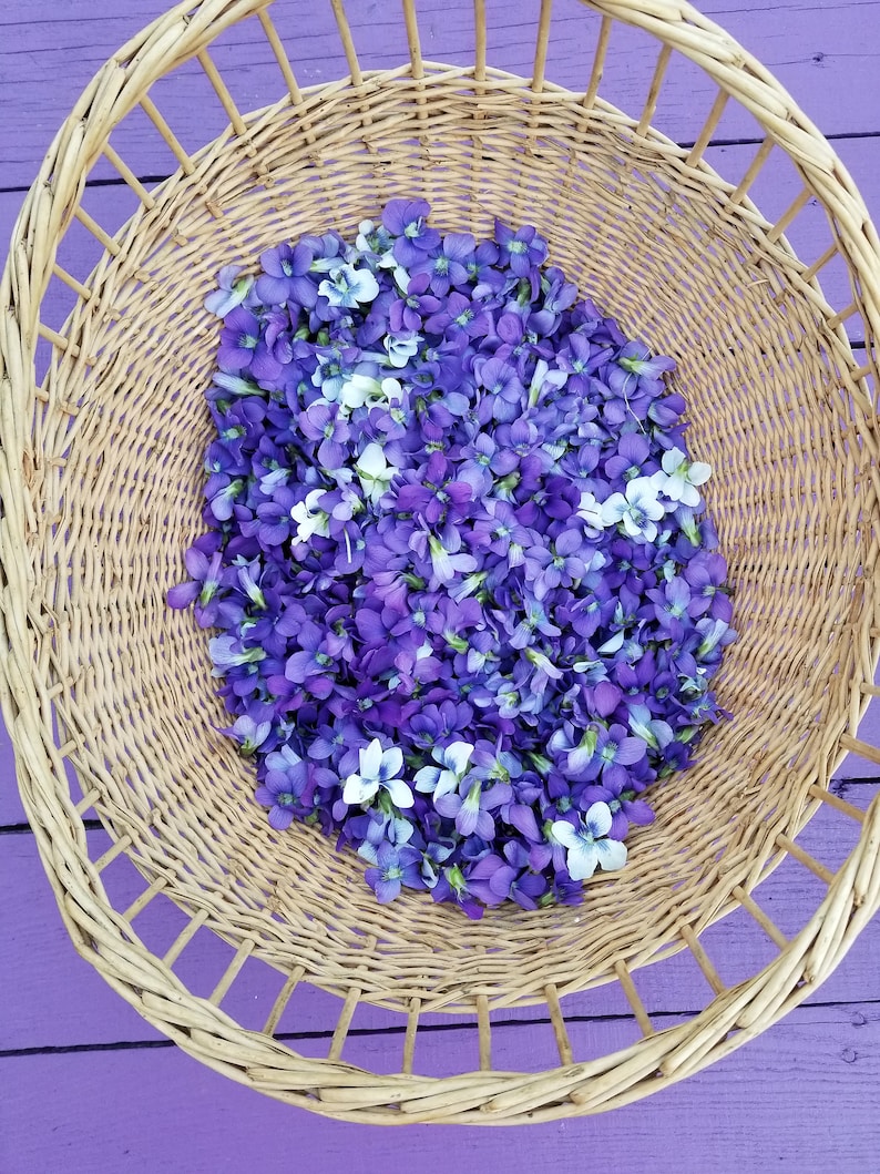 Puede incluir: Una cesta de mimbre llena de flores violetas y blancas. La cesta est&aacute; sobre una superficie morada.