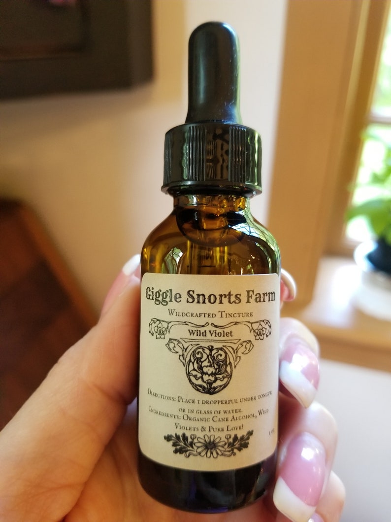 Puede incluir: Una botella de vidrio con un gotero, etiquetada como "Giggle Snorts Farm Wildcrafted Tincture Wild Violet". La etiqueta tambi&eacute;n incluye instrucciones de uso e ingredientes, que son "Alcohol de ca&ntilde;a org&aacute;nica, Violetas silvestres y Amor puro!"