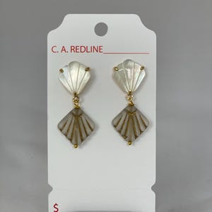 Puede incluir: Pendientes colgantes con diseño de concha. Los pendientes presentan una parte superior nacarada en forma de abanico y una parte inferior en forma de diamante con detalles dorados. Se exhiben en una tarjeta blanca con el texto "C. A. REDLINE".