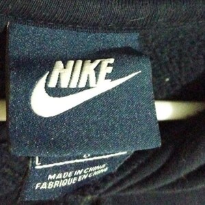 May include: A navy blue tag featuring the white Nike logo and the word "NIKE" in white block letters. Below the logo, the tag reads "MADE IN CHINA" and "FABRIQUE EN CHINE". The tag is attached to a dark blue garment.