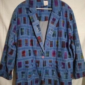 May include: A blue blazer with a repeating pattern of colorful plaid squares. The blazer has a single pink button closure and is hanging on a white hanger. The sleeves are three-quarter length.