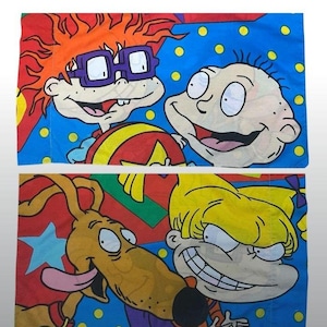 May include: Two pillowcases featuring cartoon characters. One pillowcase has Chuckie and Tommy on a blue background with yellow polka dots. The other pillowcase has Spike and Angelica on a red and blue background.