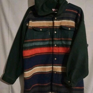 May include: A hooded button-up jacket with a striped pattern in shades of green, red, blue, and tan. The sleeves and hood are a solid dark green. The jacket has two chest pockets and is hanging on a white hanger.