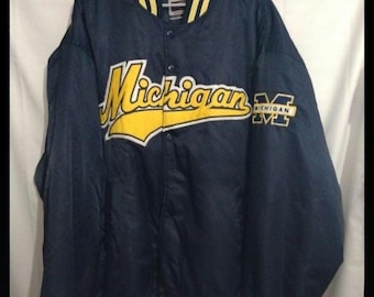 May include: Navy blue satin jacket with yellow accents. The word "Michigan" is prominently displayed across the chest in yellow script, with a matching "M" logo on the sleeve. The collar, cuffs, and hem feature yellow stripes.