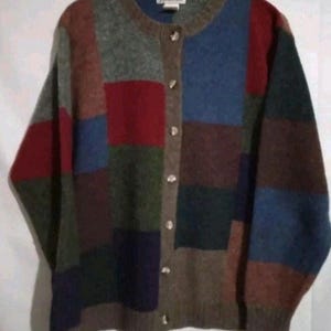 May include: A patchwork cardigan in various colours, including red, blue, green, and brown, with a round neck and button closure. The label reads "Oasis". The sweater is a cozy, textured knit.