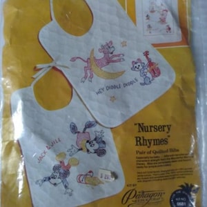 May include: A vintage "Nursery Rhymes" cross-stitch kit featuring two quilted bibs with Disney character designs. One bib has "Jack & Jill" and Mickey Mouse, the other has "Hey Diddle Diddle" with a cow and moon.