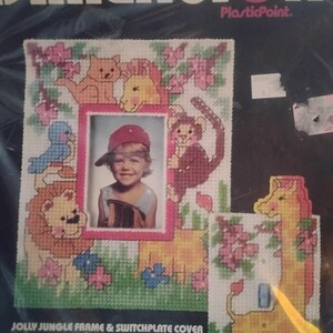 May include: A Dimensions plastic canvas kit for a Jolly Jungle frame and switchplate cover. The frame features a photo of a child, surrounded by stitched jungle animals and flowers. The switchplate cover has a giraffe design.