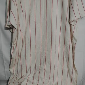 May include: Cream-colored, short-sleeved shirt with vertical red stripes. The fabric appears to be lightweight and slightly wrinkled. The shirt is a casual style, suitable for everyday wear.